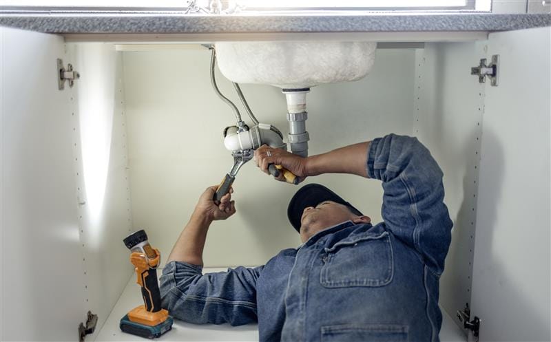 Plumber repairing pipes beneath a bathroom sink in Newnan