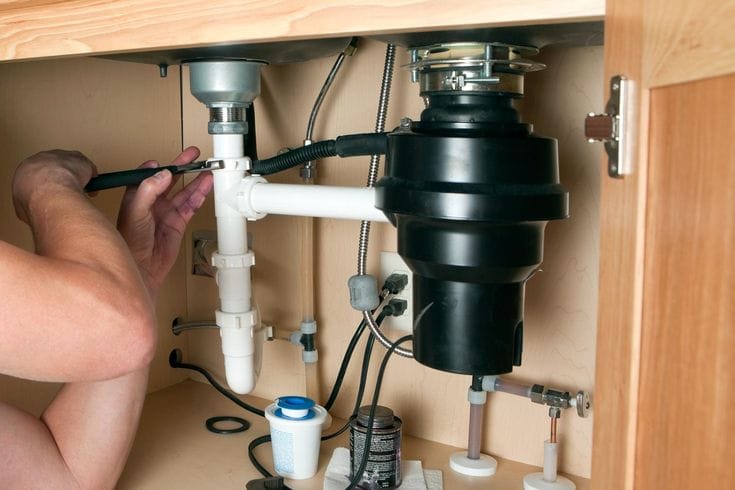 Plumber installing a garbage disposal beneath a kitchen sink in Newnan