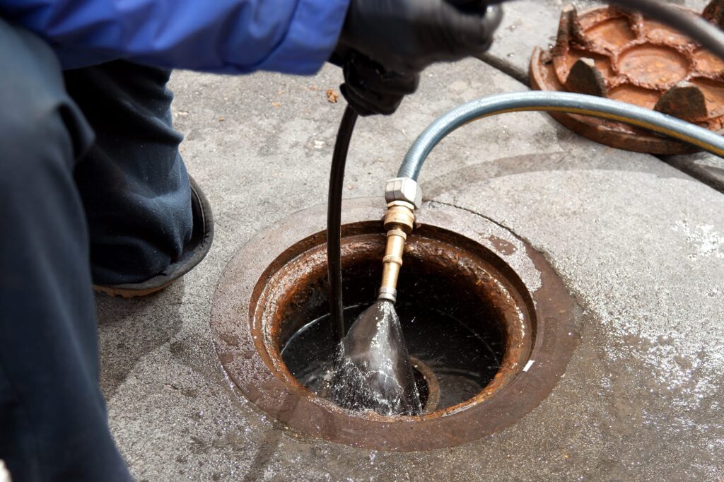 Plumber hydro jetting a sewer line through a manhole in Newnan