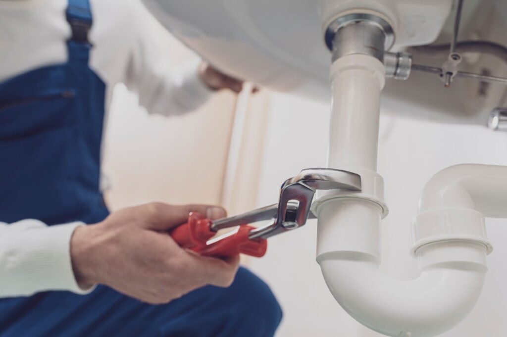 Plumber repairing a white drain pipe beneath a sink in Newnan