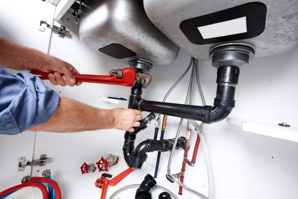 Plumber repairing drain pipes beneath a kitchen sink in Newnan